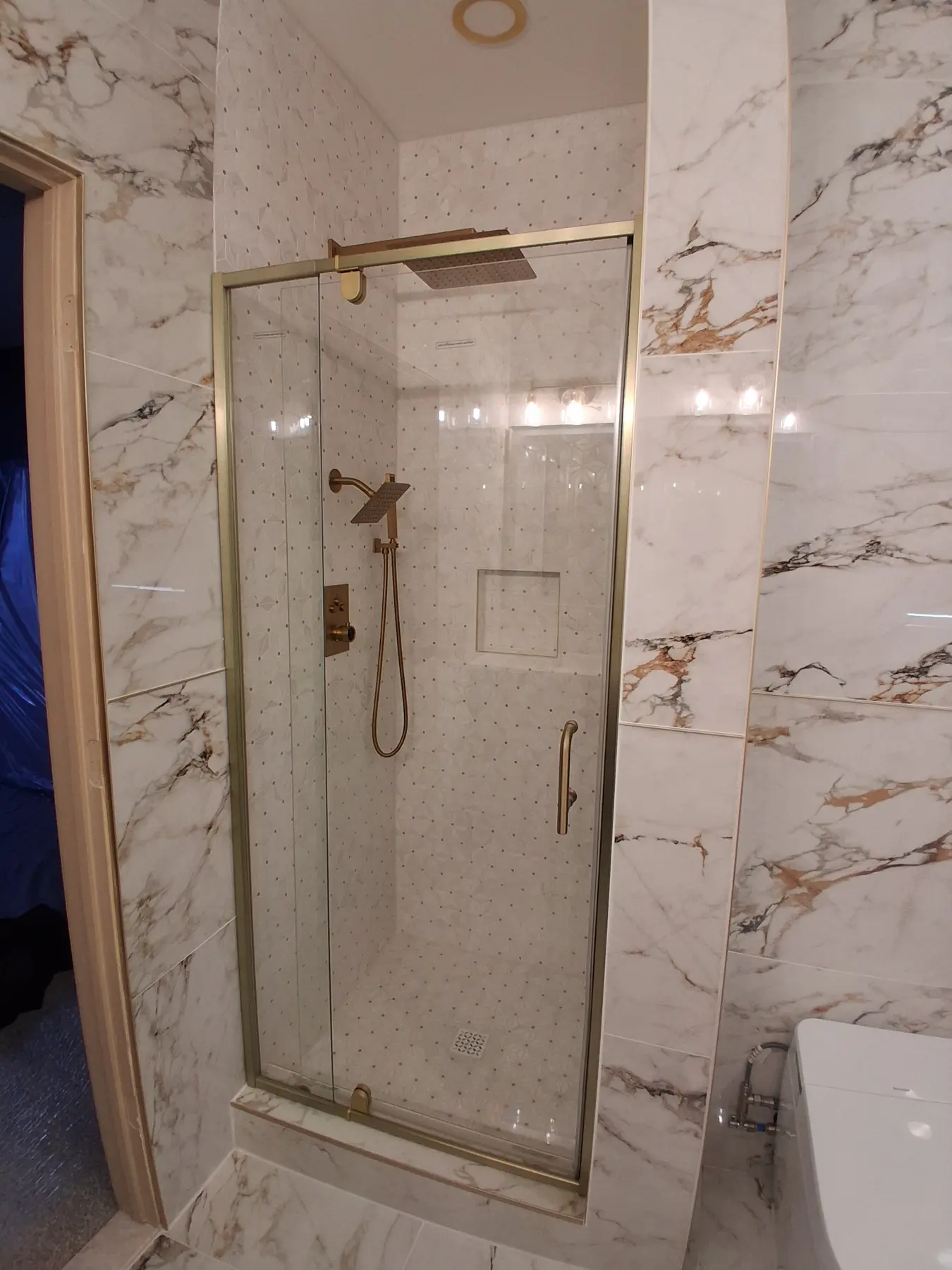 Walk-in shower with brushed gold rain head, handheld and glass door, tiled in a white and gold mosaic