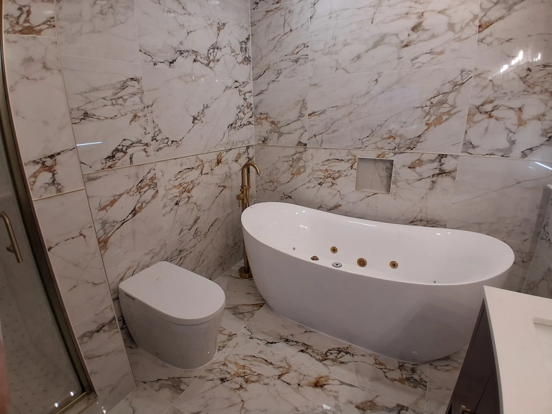 Primary bath in Calacatta-gold tile with a freestanding jetted tub and a brushed gold floor-mount filler