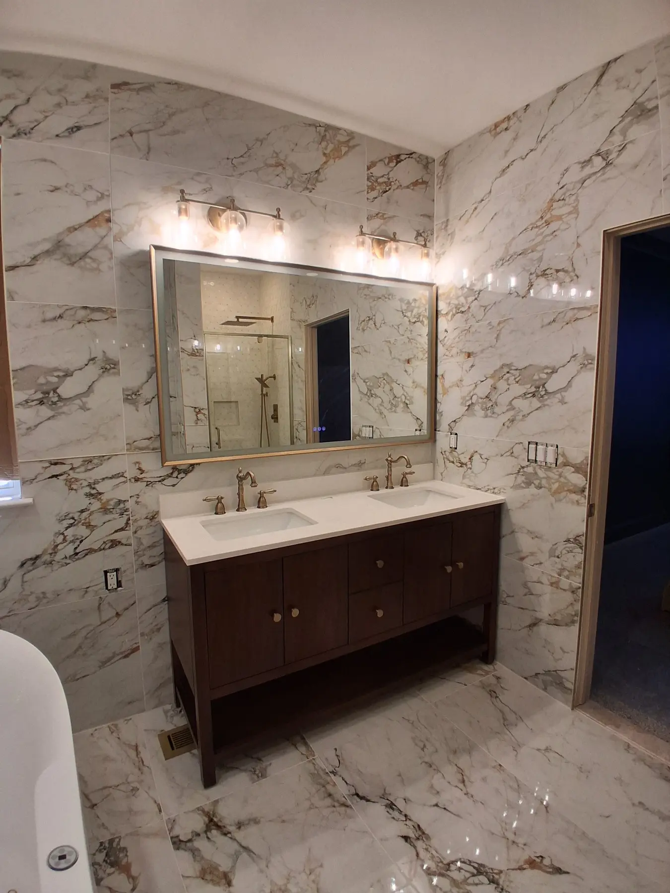 Double vanity in dark wood with a white quartz top, brushed gold faucets, an LED mirror and glass sconces