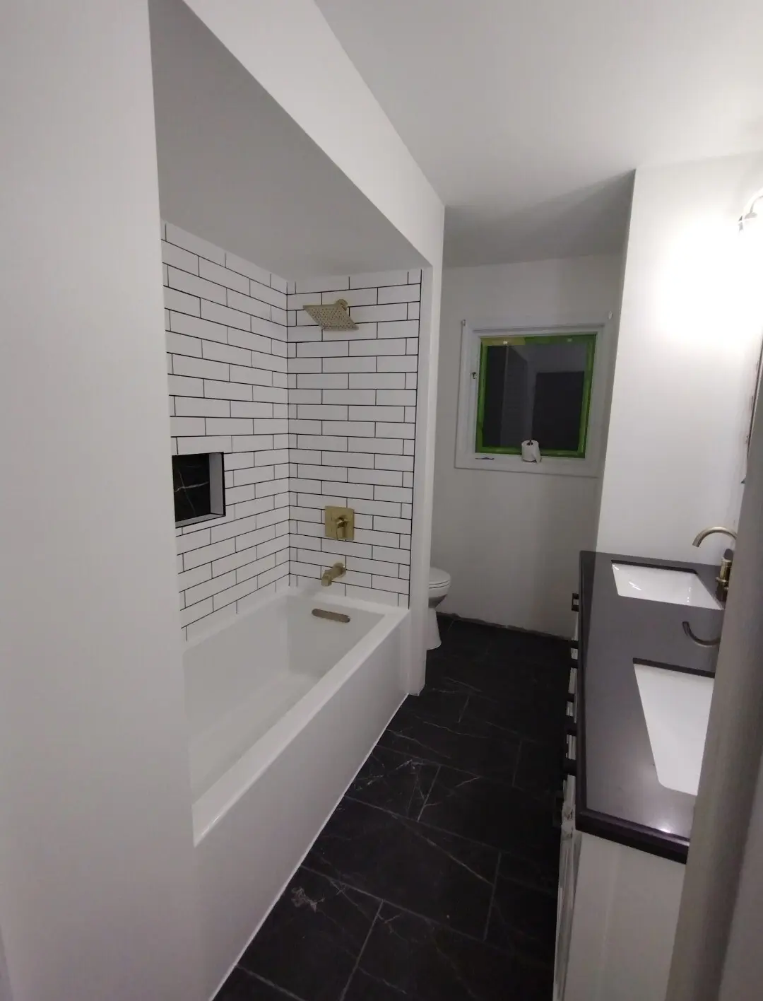 Guest bath with white subway tile and black grout, a black marble floor and brass fixtures